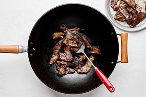 steak tossed with Shaoxing wine, salt, soy sauce, dark soy sauce, and cornstarch being cooked in a skillet