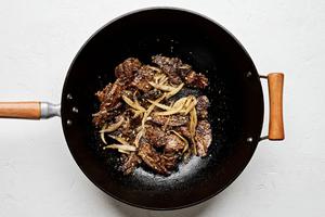 Flank steak added to a skillet with onion, garlic, ginger and peppercorns