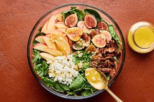 spinach, arugula, goat cheese, apples, figs and candied pecans in a bowl being drizzled with a citrusy dijon vinaigrette