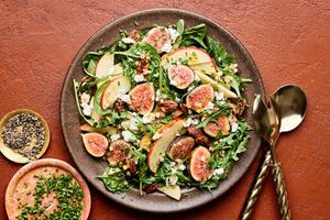 A fig and goat cheese salad in a bowl with a citrusy dijon vinaigrette next to bowls of chives and pepper for topping
