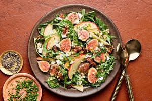 A fig and goat cheese salad in a bowl with a citrusy dijon vinaigrette next to bowls of chives and pepper for topping