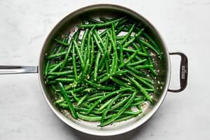 blanched green beans being cooked in a skillet with olive oil, garlic, salt & pepper