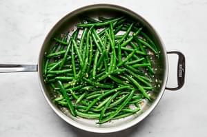 blanched green beans being cooked in a skillet with olive oil, garlic, salt & pepper