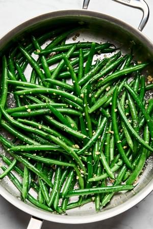 blanched green beans being cooked in a skillet with olive oil, garlic, salt & pepper
