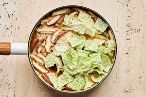 cabbage being added to a pot of gingery vegetable soup