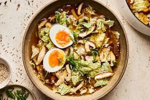 a bowl of gingery vegetable soup topped with green onions, sesame seeds and boiled eggs