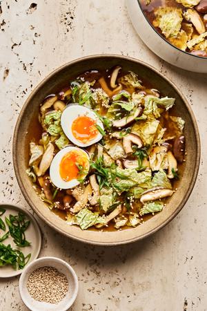 a bowl of gingery vegetable soup topped with green onions, sesame seeds and boiled eggs