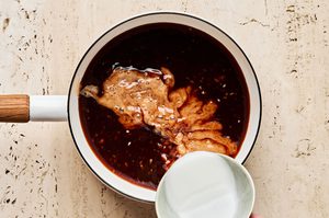 a cornstarch being added to a small sauce pan of sweet and smoky huli huli sauce to thicken it