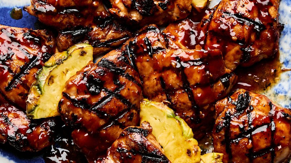 A plate of juicy huli huli grilled chicken served with fresh pineapple slices, a Hawaiian-style meal