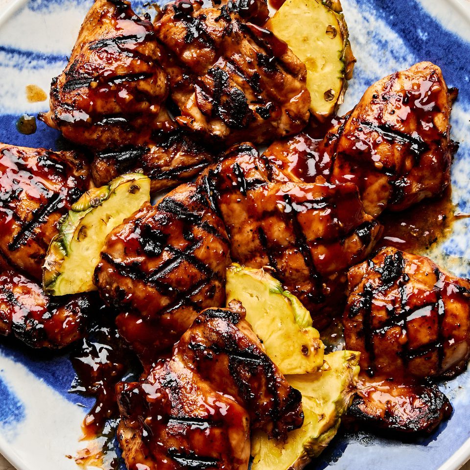 A plate of juicy huli huli grilled chicken served with fresh pineapple slices, a Hawaiian-style meal