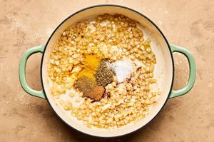 garam masala, cumin, turmeric, cinnamon, and salt being added to a pot with cooked onion