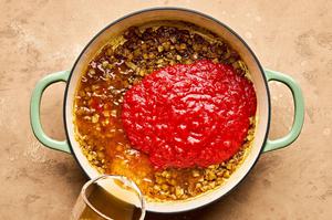 crushed tomatoes and chicken stock being added to a pot with cooked onion and spices