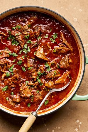 lamb curry cooking in a pot seasoned with garlic, garam masala, cumin, turmeric and cinnamon and sprinkled with cilantro