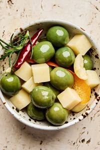 a bowl of green olives and diced Gruyère marinated in garlic, orange, rosemary, peppercorn, dried chili and olive oil