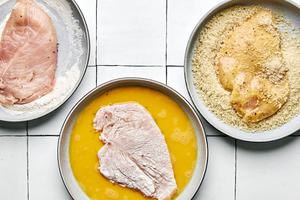 butterflied chicken seasoned with salt and pepper being dredged in flour, eggs and panko breadcrumbs