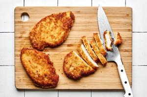panko chicken made with salt, pepper, eggs, flour, breadcrumbs and fried in vegetable oil being sliced on a cutting baord