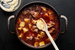 A flour paste being stirred into a pot of pork stew with a wooden spoon
