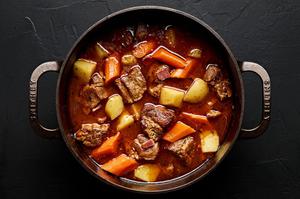 a pot of pork stew made with potatoes, carrots, onion, carrots, bacon, spices and tomato paste