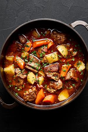 a pot of pork stew made with potatoes, carrots, onion, carrots, bacon, spices and tomato paste sprinkled with parsley