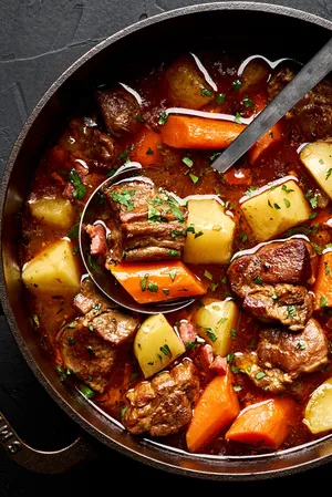 a pot of pork stew made with potatoes, carrots, onion, carrots, bacon, spices and tomato paste sprinkled with parsley