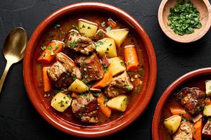 a bowl of pork stew made with potatoes, carrots, onion, carrots, bacon, spices and tomato paste sprinkled with parsley