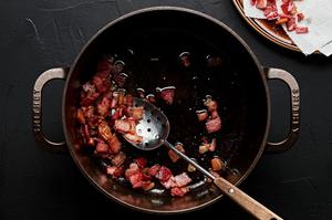 chopped bacon cooked in a pot being spooned out on a paper towel lined plate to drain