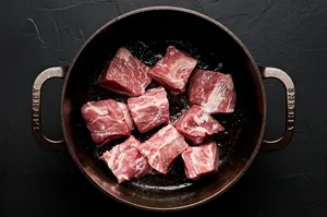 pork pieces being browned in a soup pot
