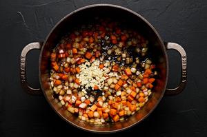 onion, garlic, and carrots being cooked in olive oil in a soup pot