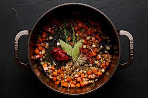 tomato paste, bay leaves, thyme, paprika, and Italian seasoning being stirred in to a pot with onion, carrots and garlic