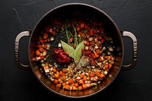 tomato paste, bay leaves, thyme, paprika, and Italian seasoning being stirred in to a pot with onion, carrots and garlic