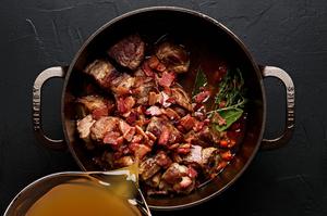 broth being poured into a soup pot with cooked vegetables and spices