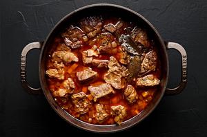 browned pork and cooked bacon being added to a pot of stew