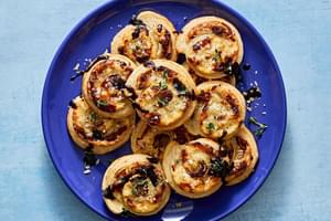 plate of puff pastry pinwheels filled with cream cheese, swiss, caramelized onions & spices drizzled with balsamic glaze