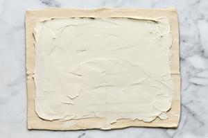 cream cheese being spread onto unbaked puff pastry