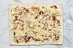 puff pastry being filled with cream cheese, Swiss, caramelized onions, dijon & thyme being sliced into pinwheels