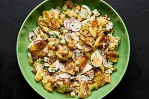 a bowl of smashed potato salad made with boiled eggs, cucumber, pickles, chives, parsley and a mayo based dressing