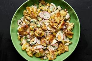 a bowl of smashed potato salad made with boiled eggs, cucumber, pickles, chives, parsley and a mayo based dressing