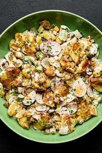 a bowl of smashed potato salad made with boiled eggs, cucumber, pickles, chives, parsley and a mayo based dressing