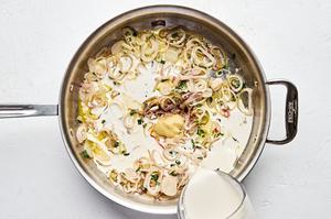 heavy cream being poured into a skillet with heavy creambutter, shallots, spices, Gruyere and Parmesan