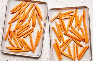 sweet potatoes tossed with olive oil on a parchment paper lined baking sheet