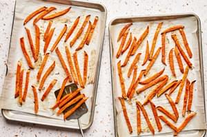 sweet potatoes fries being scooped off a parchment paper lined baking sheet