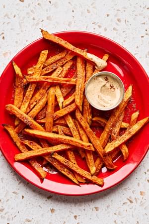 sweet potato fries on a red plate seasoned with brown sugar, garlic powder, chili powder, salt, pepper with chipotle mayo
