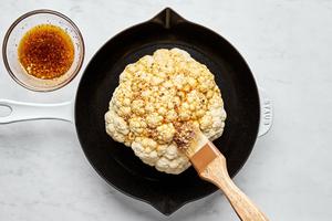 a head of cauliflower being brushed with olive oil, garlic, Italian seasoning, salt, paprika and pepper