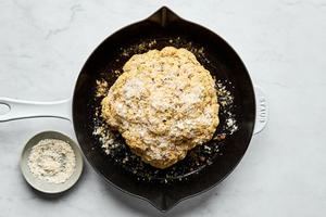 an Italian seasoned head of cauliflower in a cast iron skillet being sprinkled with Parmesan cheese
