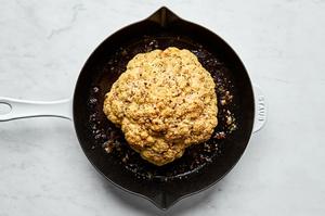 a whole roasted cauliflower in a skillet seasoned with italian seasoning, garlic and salt, topped with Parmesan cheese