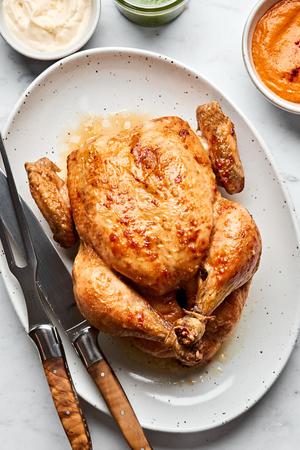 a whole roasted chicken on a serving plate with a carving knife served with romesco sauce, pesto and garlic aioli for dipping