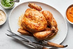 a whole roasted chicken on a serving plate with a carving knife served with romesco sauce, pesto and garlic aioli for dipping