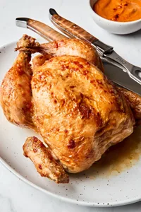 a whole roasted chicken on a serving platter with a carving knife served with romesco sauce