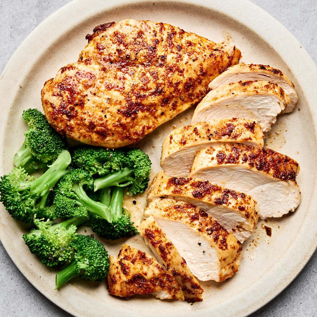 Air fryer chicken breasts cooked until golden sliced on a plate served with steamed broccoli