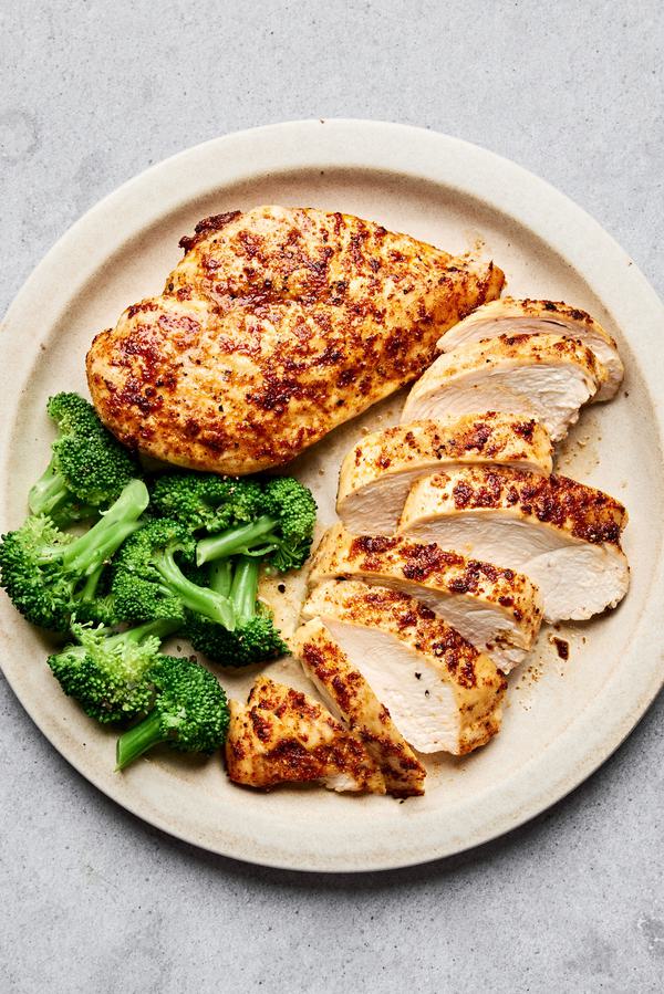 Air fryer chicken breasts cooked until golden sliced on a plate served with steamed broccoli